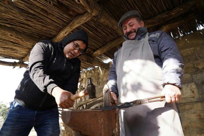 Deux artisans bâtiment préparant du mortier avec outils traditionnels sous un abri de chantier.