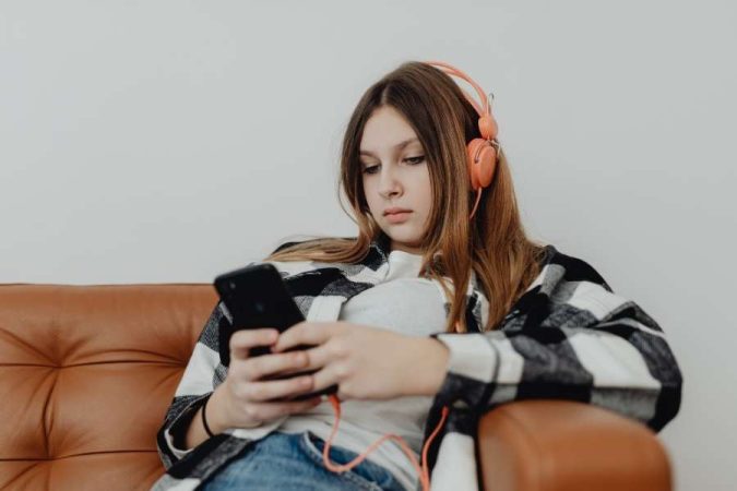 Jeune femme décontractée écoutant de la musique en streaming sur smartphone avec casque orange