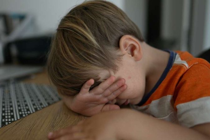Un jeune enfant timide cache son visage avec sa main, illustrant la timidité chez les plus jeunes.