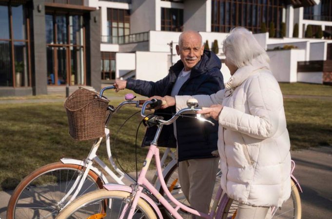 Couple de seniors à vélo devant un ensemble résidentiel moderne, illustrant l'impact vieillissement population immobilier.